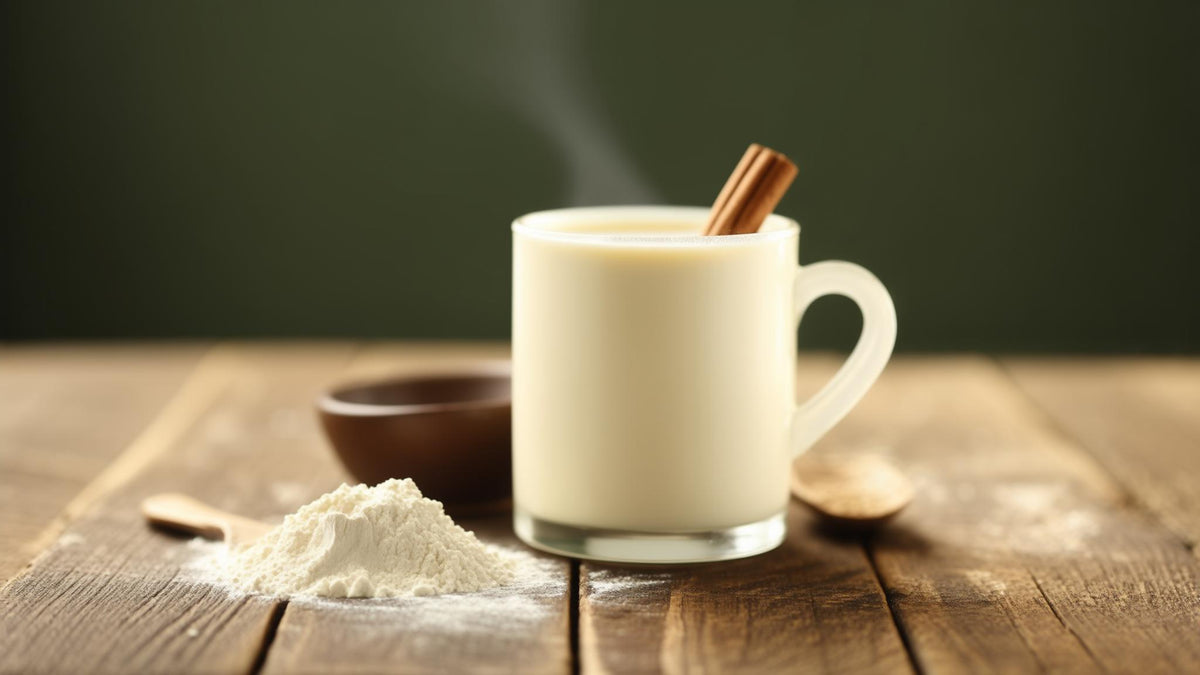 A mug of warm milk with cinnamon beside a bowl of colostrum powder on a wooden table