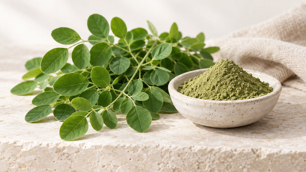 Fresh green leaves beside a stone bowl of green leaf powder on a pale stone surface