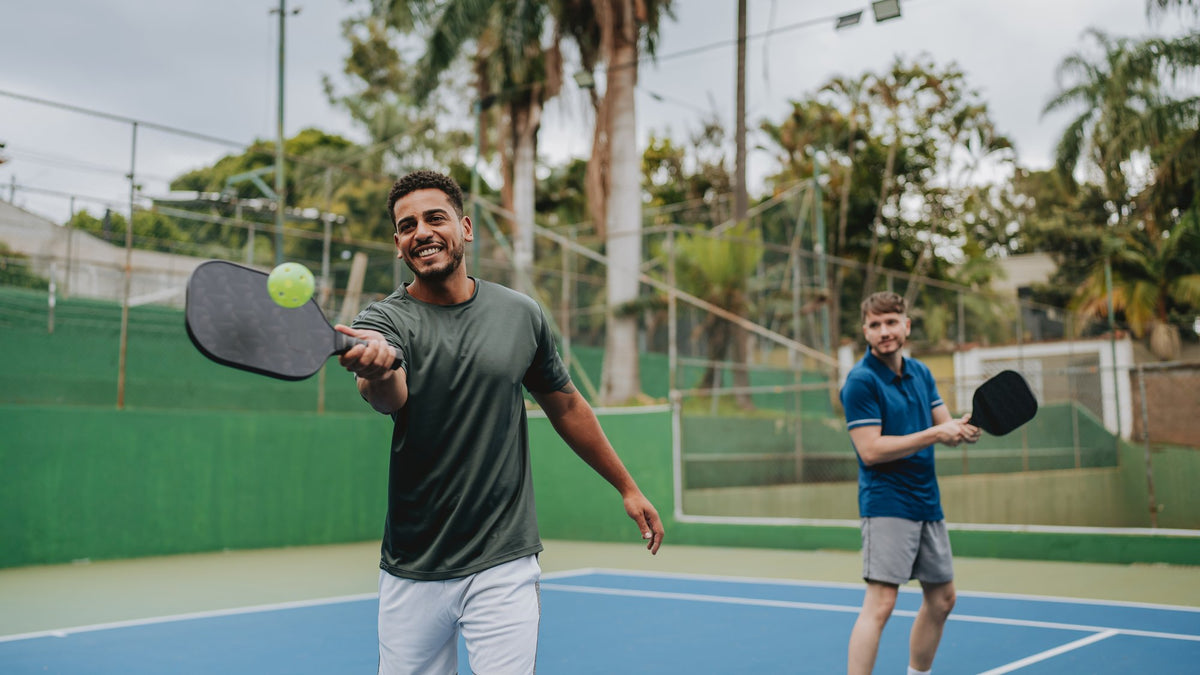 Two men playing pickleball on an outdoor court on a sunny day, one returning the ball