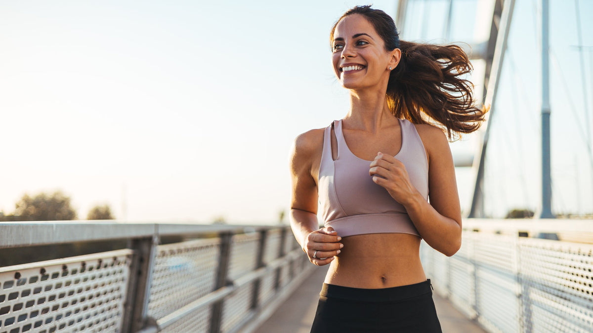 Smiling woman jogging across a footbridge at golden hour