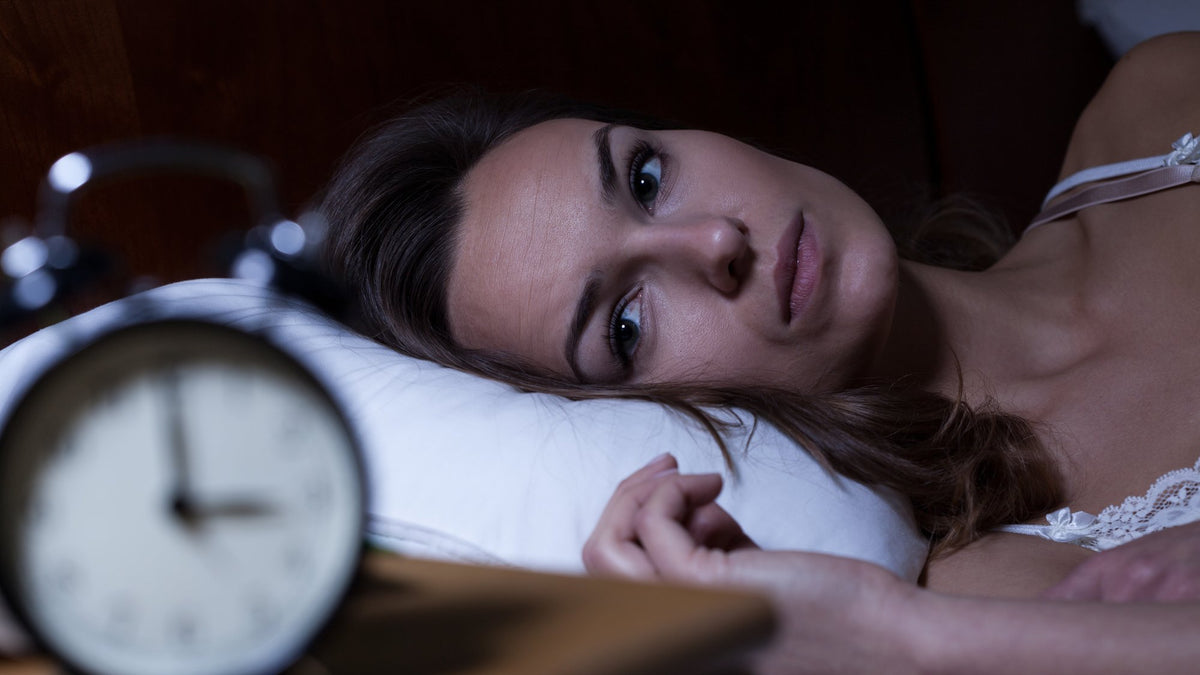 A person lying awake in bed at night, looking past a blurred alarm clock that shows about 3 o'clock