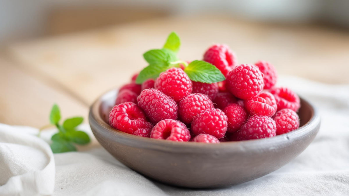 A bowl of fresh raspberries with mint leaves on pale linen