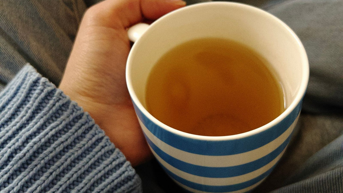 Hand in a knit sweater holding a blue-and-white striped cup of tea