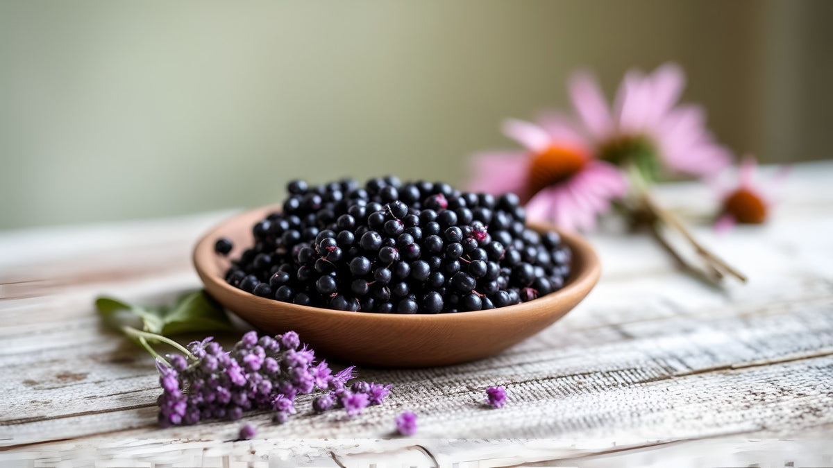 A bowl of elderberries beside purple echinacea flowers on a wooden table