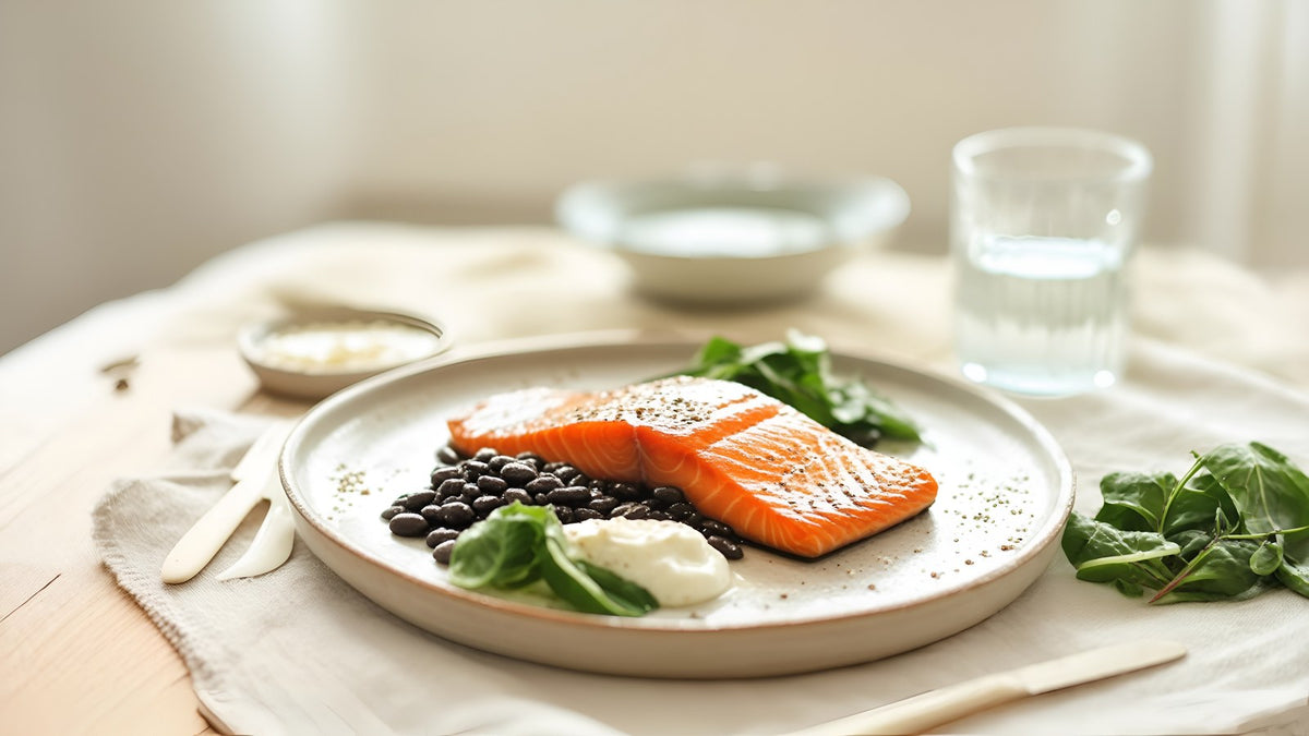 Salmon, black beans, yogurt, leafy greens and water on a wooden table, midlife nutrition basics