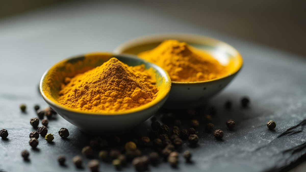 Ground turmeric beside whole black peppercorns on slate
