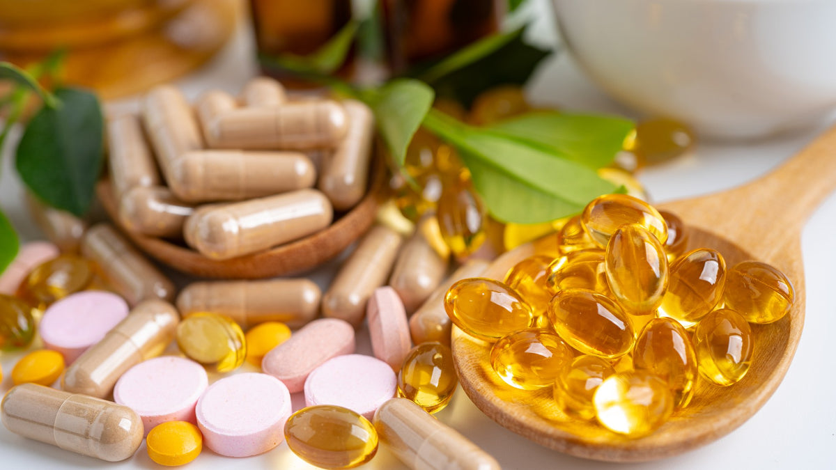 Capsules, tablets and golden softgels on a wooden spoon and a white surface