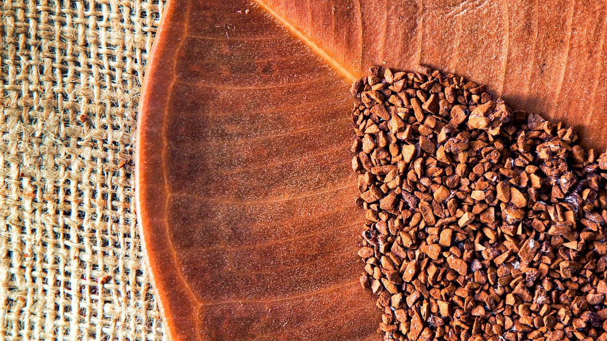 Coffee granules spilling across a large dried leaf on a woven burlap background