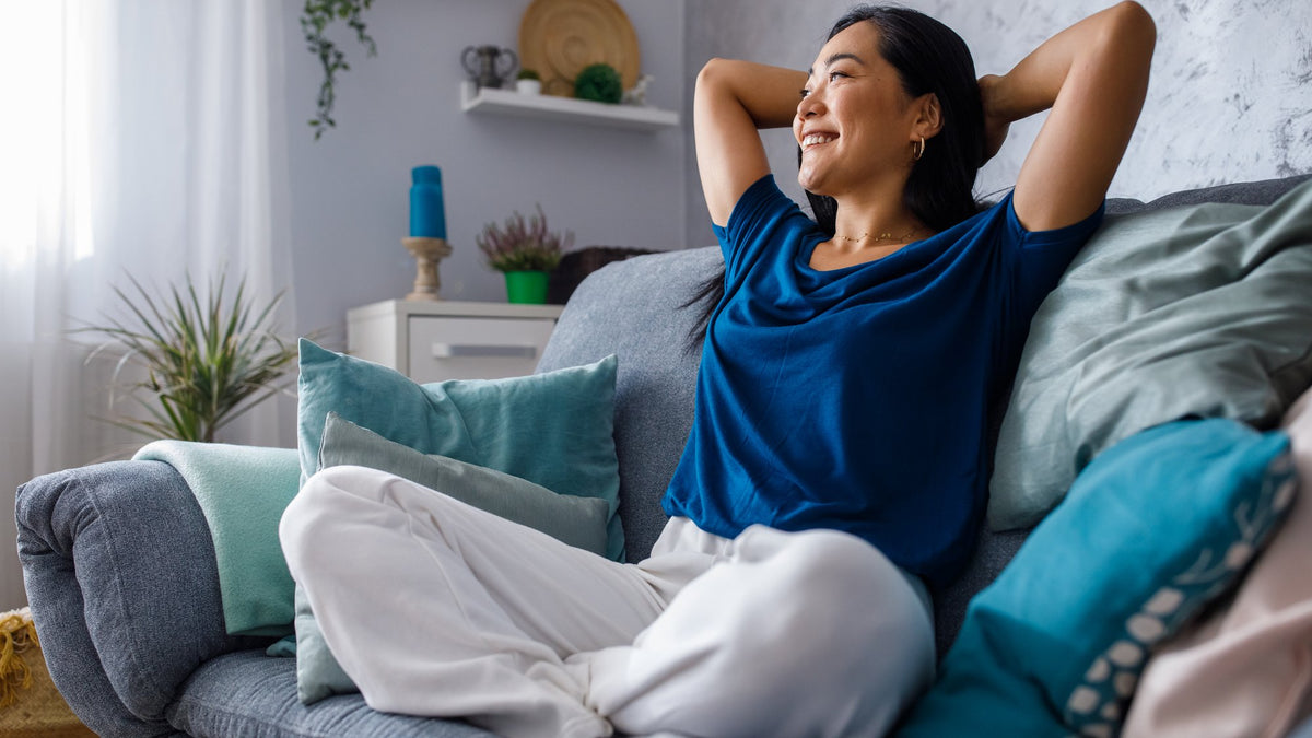 Smiling person relaxing on a blue sofa with hands behind head in a bright living room