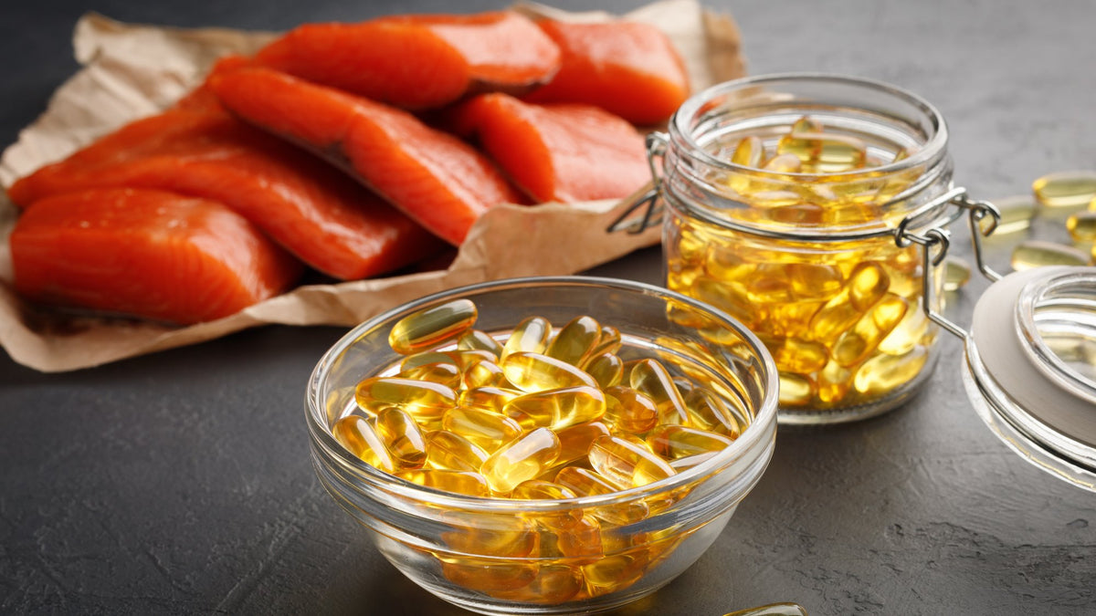 Golden omega-3 softgels in glass bowls beside raw salmon fillets on kraft paper