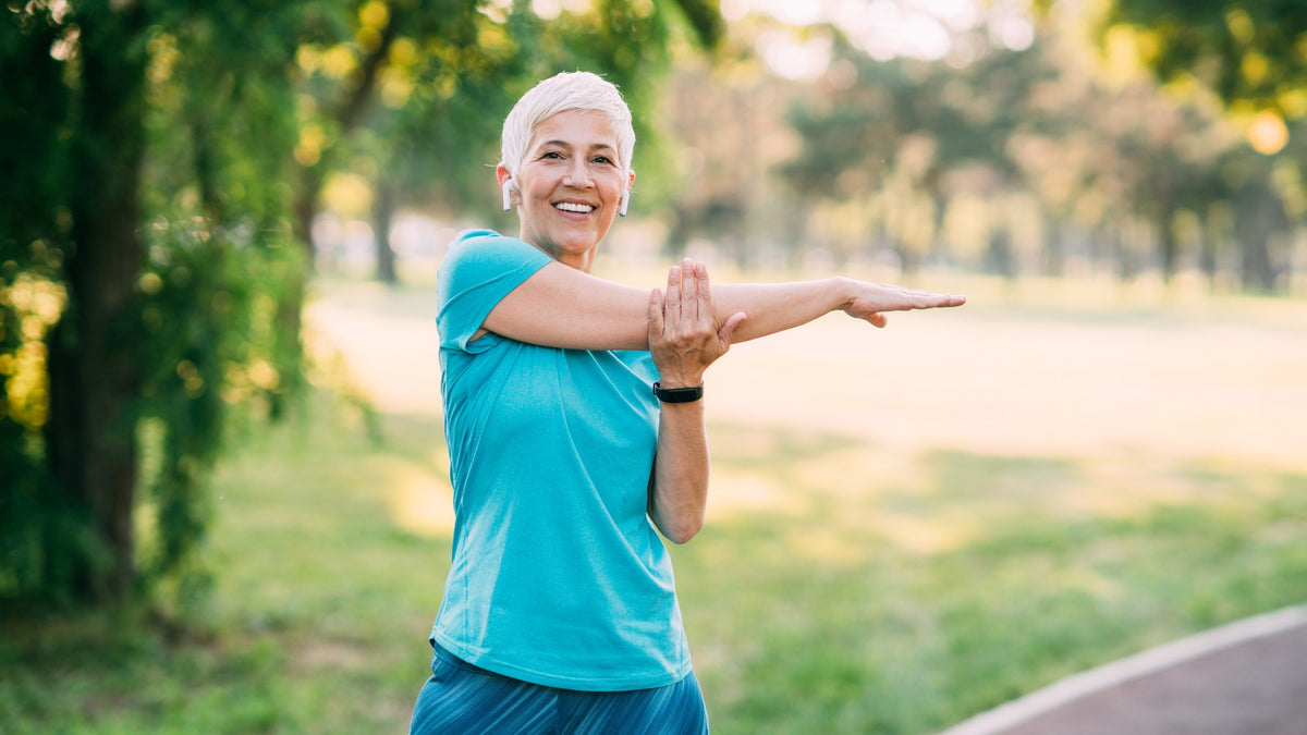 Cheerful senior woman stretching outdoors in a green park