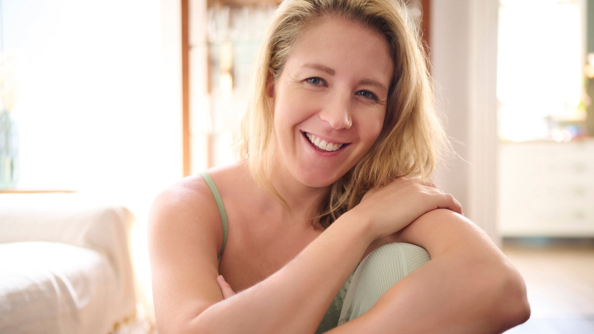 Smiling adult with natural skin and loose blonde hair, sitting at home in soft window daylight