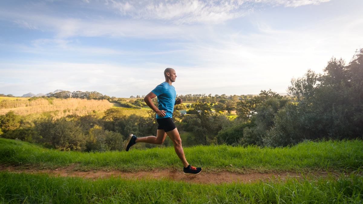 Man running along a grassy countryside trail under a wide blue sky