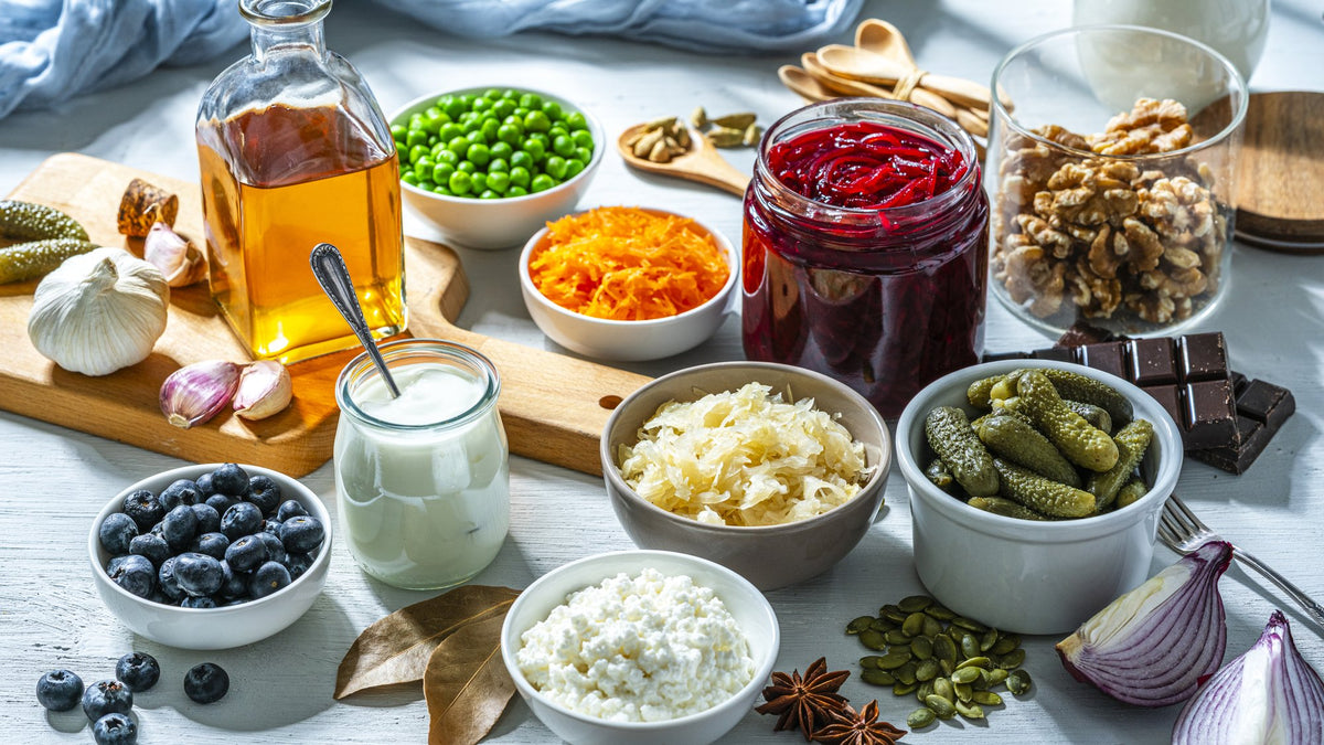 Overhead spread of fermented foods: kefir, sauerkraut, pickles, yogurt and blueberries on pale wood