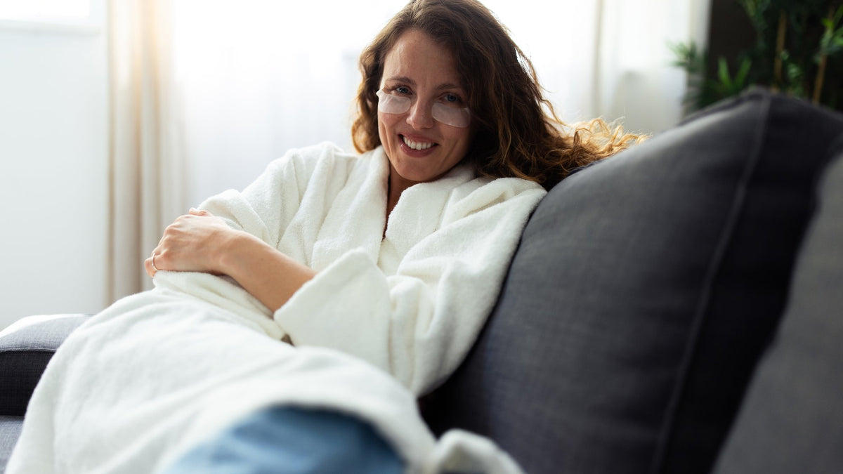 Woman in a white robe curled up on a sofa, smiling, winding down for the evening